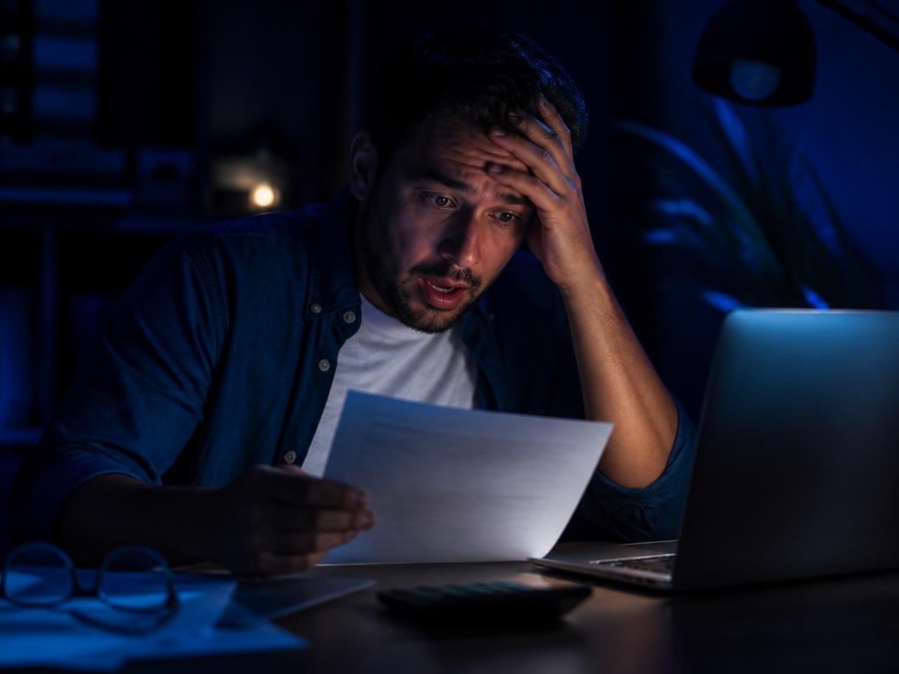 A business owner at a desk at night, holding an invoice and looking shocked